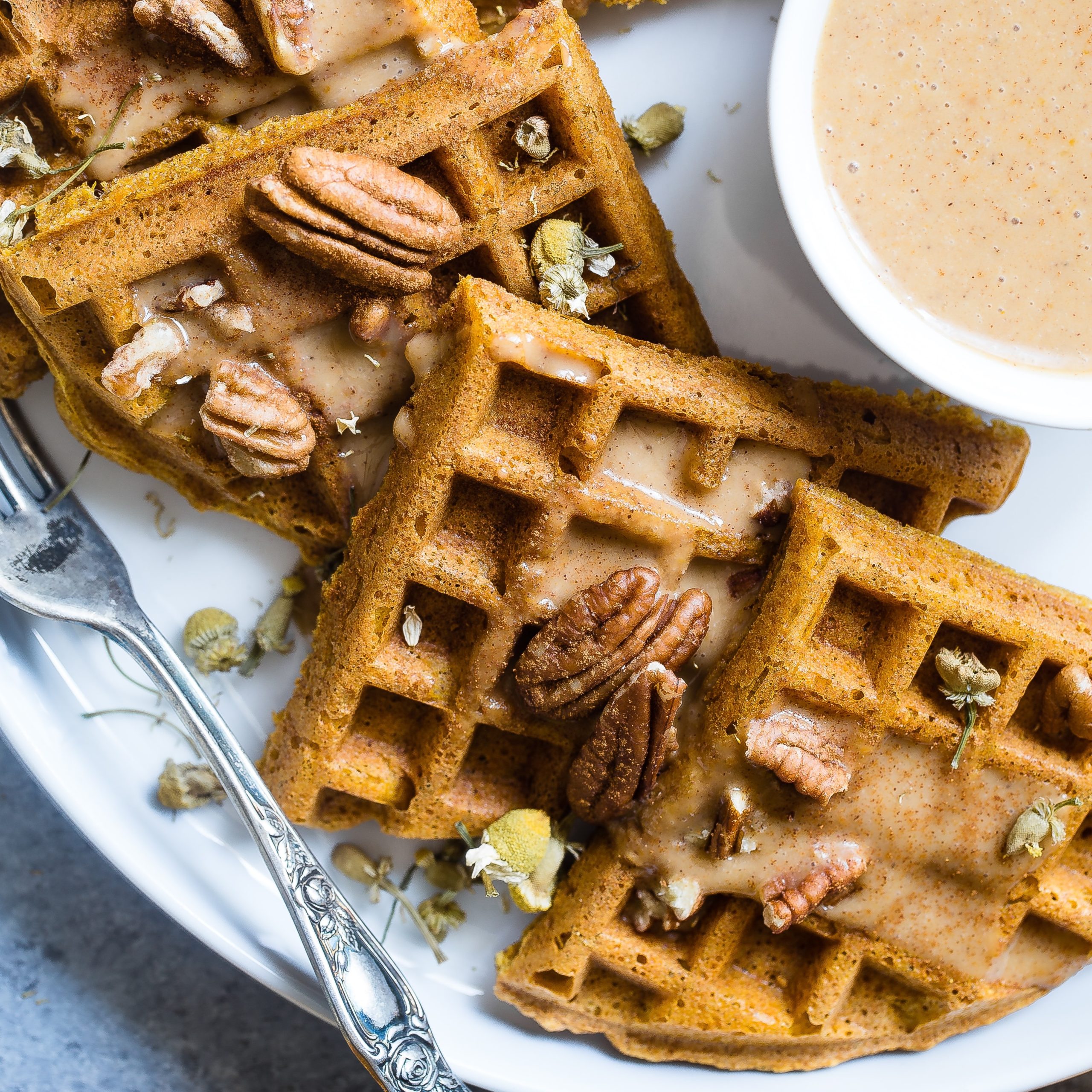 closeup of whole grain khorasan wheat sourdough waffle with pecans and butter syrup on a plate with a fork